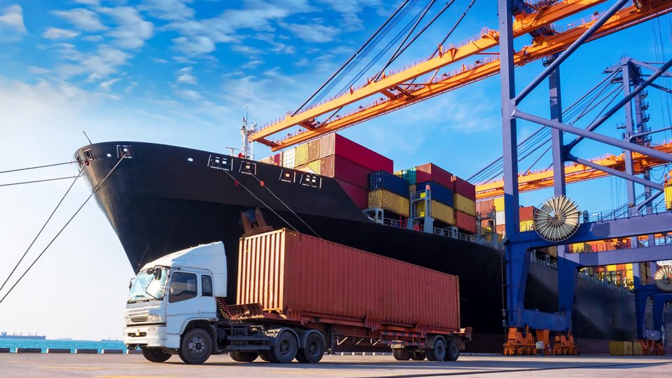 Fraktlastbil och fraktfartyg med containrar vid industriell lasthamn