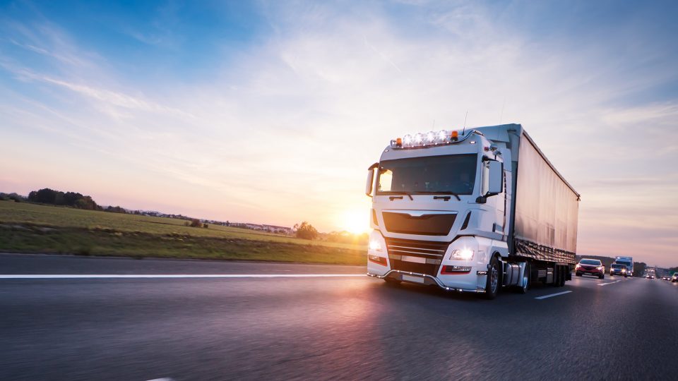 En vit lastbil körandes i solnedgång.